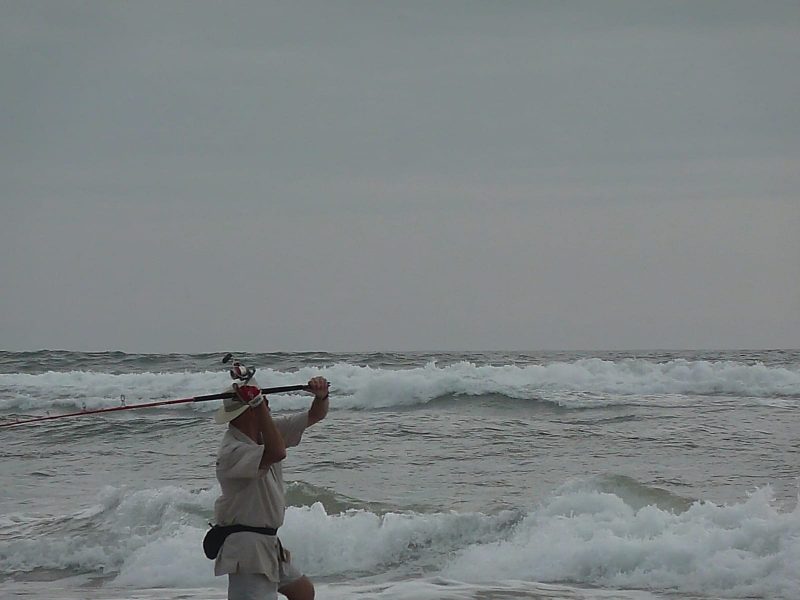 Pêcheur pratiquant le surfcasting dans les vagues de l’océan Atlantique sur une plage d’Iguéla au Gabon.
