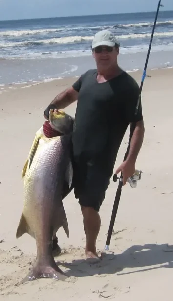 Pêcheur tenant un grand capitaine capturé de nuit sur une plage du Gabon, avec un leurre de surface visible au premier plan.
