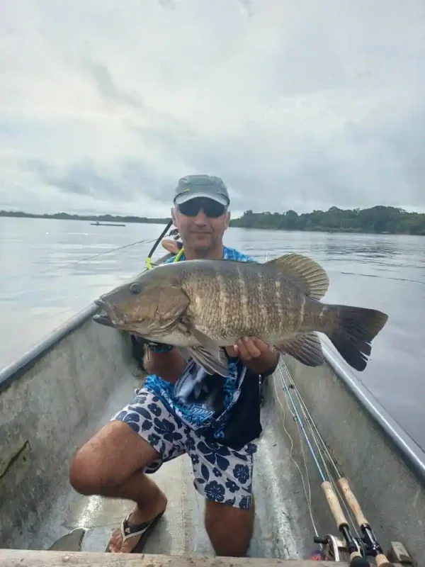 Pêcheur tenant une carpe rouge dans une embarcation sur les eaux calmes de la lagune d’Iguéla au Gabon.