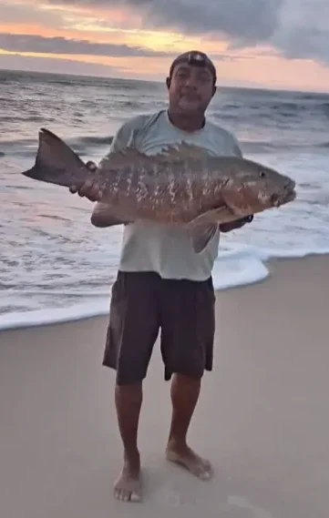Guide présentant une grande carpe rouge capturée depuis la plage dans la région d’Iguéla au Gabon.