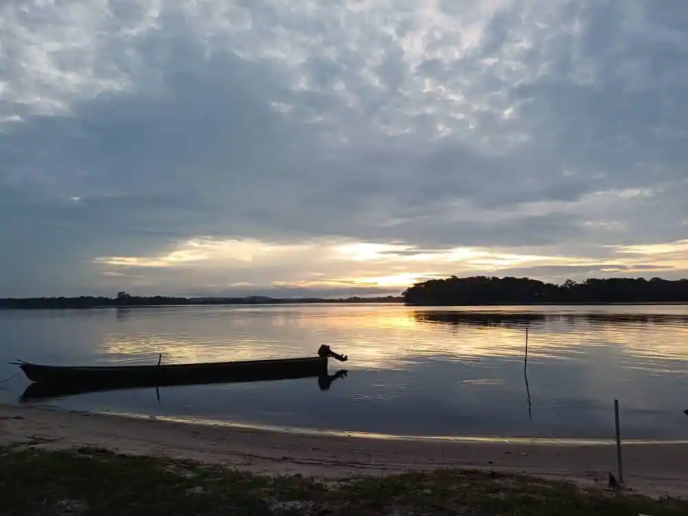 Pirogue traditionnelle au coucher du soleil sur la lagune d’Iguéla, avec reflets dorés sur l’eau calme et silhouette de la forêt tropicale du Gabon à l’horizon.