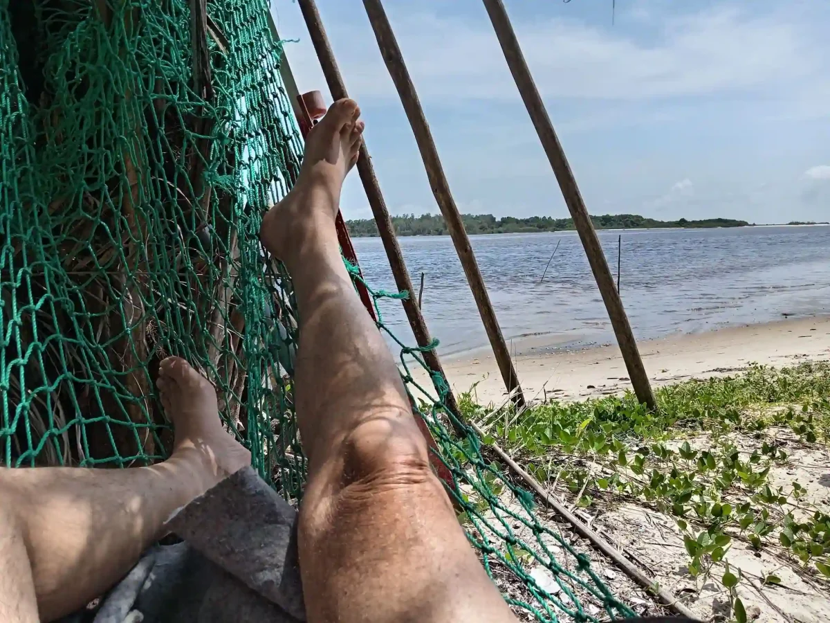Vue depuis un hamac installé au bord de la lagune d’Iguéla au Gabon, avec plage de sable, eau calme et ambiance paisible au cœur d’un environnement naturel préservé.
