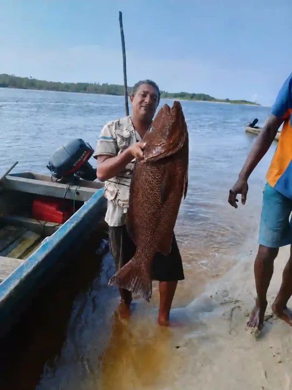 Guide de pêche présentant une grande carpe rouge capturée dans la lagune d’Iguéla au Gabon, au bord de l’eau à proximité d’une pirogue.