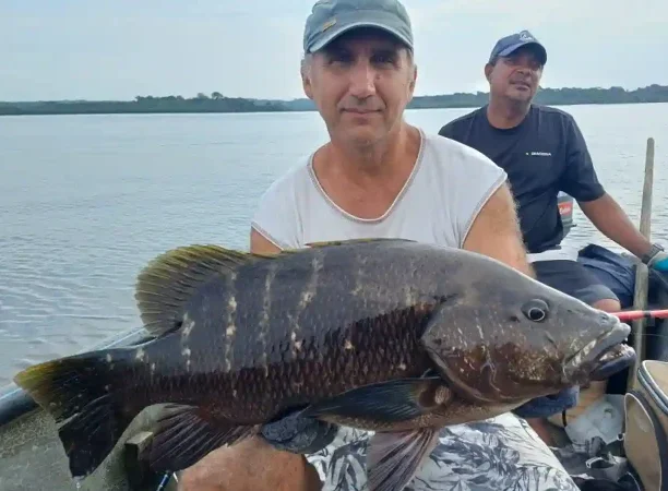 Pêcheur présentant une carpe rouge noire capturée dans la lagune d’Iguéla au Gabon, à bord d’une embarcation traditionnelle.