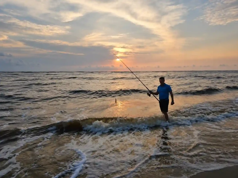 Pêcheur sportif lançant sa ligne dans les vagues de l’océan Atlantique au coucher du soleil sur les plages sauvages d’Iguéla au Gabon.