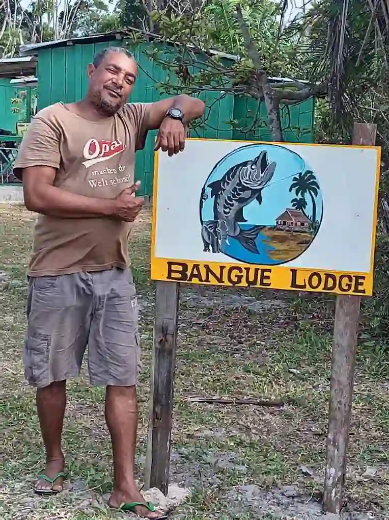 Christian, artisan pêcheur de Tchongorové, pose à côté du panneau de Bangué Lodge à Iguéla au Gabon.