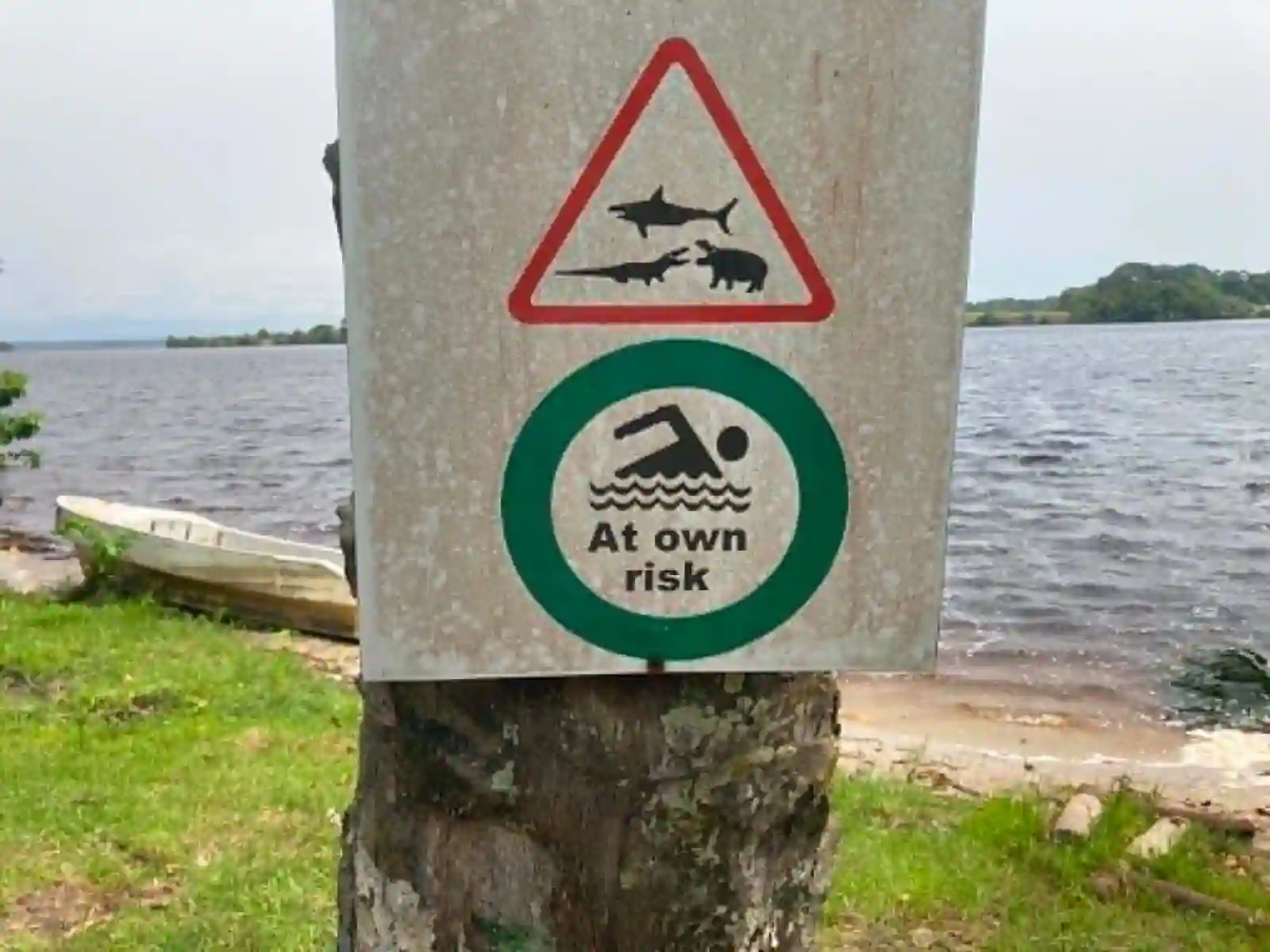 Panneau indiquant une baignade à vos risques au bord de la lagune, avec pictogrammes d’animaux sauvages.